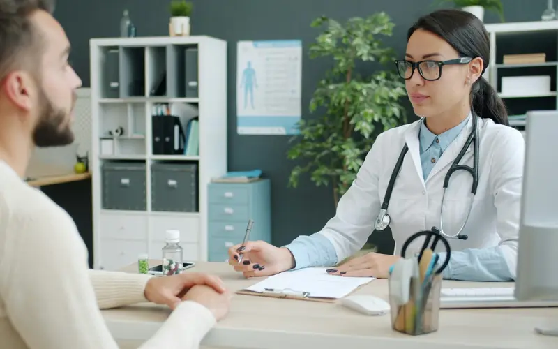 Médica do trabalho conversando com um paciente durante o atendimento no consultório.